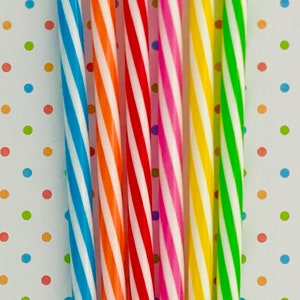 May include: A set of seven striped drinking straws in various colors, including blue, orange, red, pink, yellow, and green. The straws are arranged vertically against a white background with colorful polka dots.