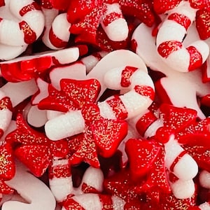 May include: A close-up of red and white candy cane and bow-shaped sprinkles. The sprinkles are covered in glitter.