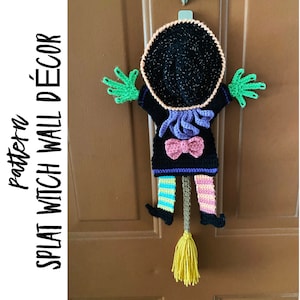 Peut inclure: Modèle de crochet pour une décoration murale de sorcière. La sorcière porte un chapeau noir avec des paillettes, une robe violette et rose et des bas rayés vert et jaune. La sorcière tient un balai jaune.