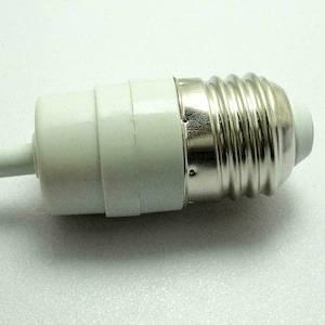May include: A white light bulb adapter with a silver screw base. The adapter has a cylindrical shape with a white plastic body and a metal base. It is designed to convert a light fixture to accommodate different bulb types.