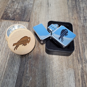 May include: A silver lighter with a black buffalo logo in a black case, next to a wooden grinder with a buffalo logo.