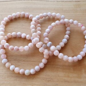May include: Three pink gemstone bracelets with round beads. The bracelets are made of light pink and white stones.