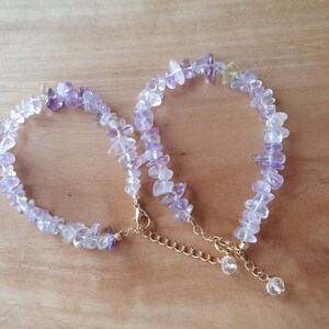 May include: Two delicate bracelets made with small, irregular amethyst and clear quartz stones. The bracelets are connected by a gold chain.