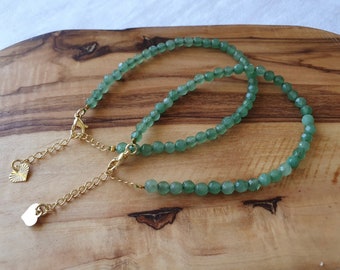 May include: Two green gemstone bracelets with gold heart charms and lobster claw clasps. The bracelets are on a wooden surface.