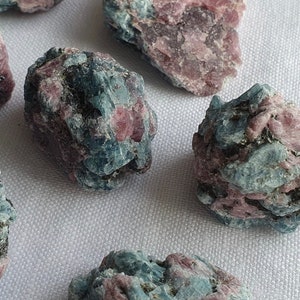 May include: A collection of six blue and pink rough gemstones. The stones are irregularly shaped and have a natural, unpolished finish.
