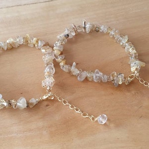 May include: Two delicate gold chain bracelets with clear quartz chips. The bracelets are connected by a small gold chain with a clear quartz charm.