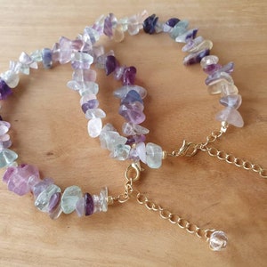 May include: Two delicate necklaces made with multi-colored fluorite gemstone chips. The necklaces are connected by a gold chain with crystal accents.