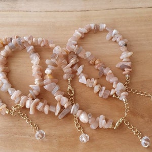 May include: Three sunstone chip bracelets with gold chain and crystal accents. The bracelets are stacked on a wooden surface.