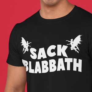 May include: Black t-shirt featuring the white text "SACK BLABBATH" and two white winged figures. The short-sleeved shirt is made of a soft material. The background is a solid red colour.