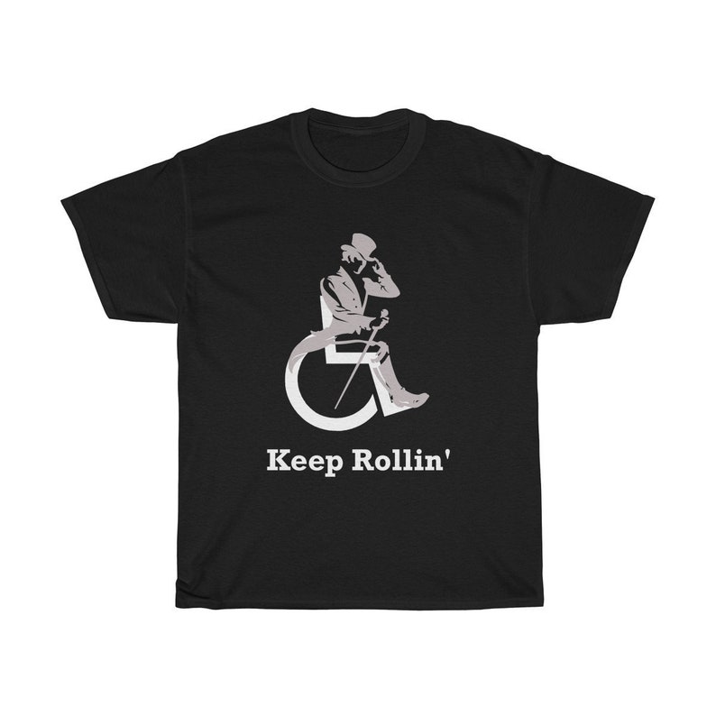 Puede incluir: Camiseta negra con una silueta blanca de una persona en silla de ruedas con un sombrero de copa y un bast&oacute;n. El texto "Keep Rollin'" est&aacute; impreso en blanco debajo de la imagen.