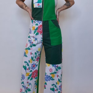 May include: Green and white patchwork overalls with a floral print. The overalls have a zipper down the front and two pockets on the front.