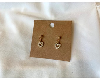 May include: A pair of gold earrings with a dangling heart charm. The heart is encrusted with clear rhinestones.