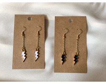 May include: Two pairs of dangle earrings with a lightning bolt charm. One pair has a white lightning bolt charm and the other pair has a black lightning bolt charm.