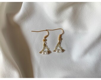 May include: A pair of gold earrings with a delicate chain and three small white pearls hanging from each earring.