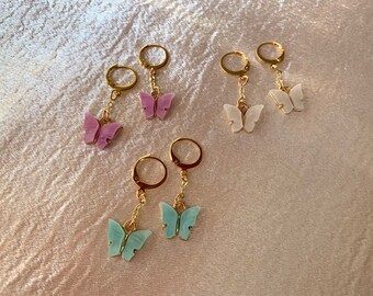 May include: A set of six gold hoop earrings with dangling butterfly charms. The butterflies are in three colors: light blue, white, and purple.