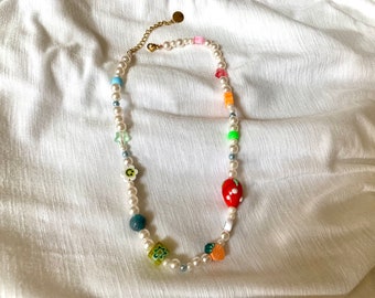 May include: A white pearl necklace with colorful charms, including a red strawberry, a green flower, a blue square, and a yellow smiley face.