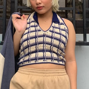 May include: A crocheted halter top with a plaid pattern in shades of cream, blue, and purple. The top has a v-neck and a collar.