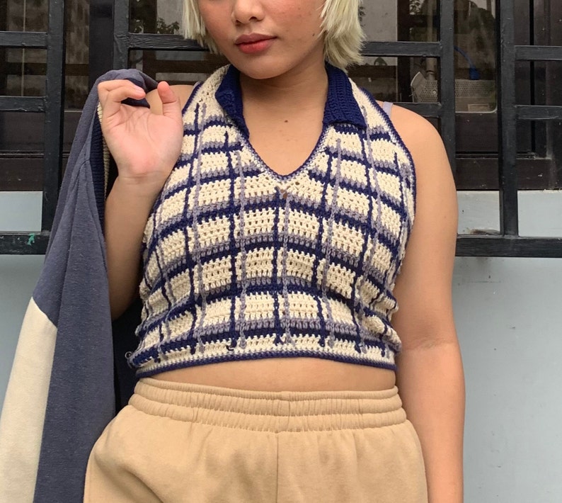 May include: A crocheted halter top with a plaid pattern in shades of cream, blue, and purple. The top has a v-neck and a collar.