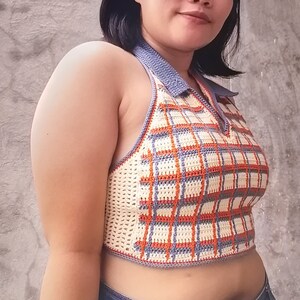 May include: A crocheted halter top with a plaid pattern in shades of orange, white, and blue. The top has a gray trim and a halter neck.