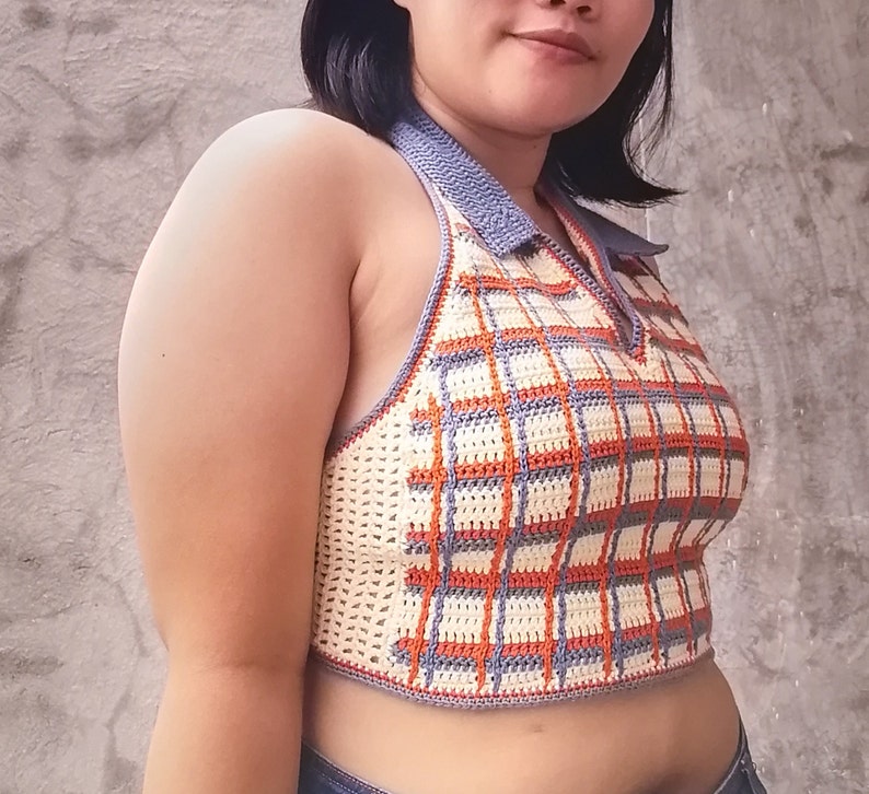May include: A crocheted halter top with a plaid pattern in shades of orange, white, and blue. The top has a gray trim and a halter neck.