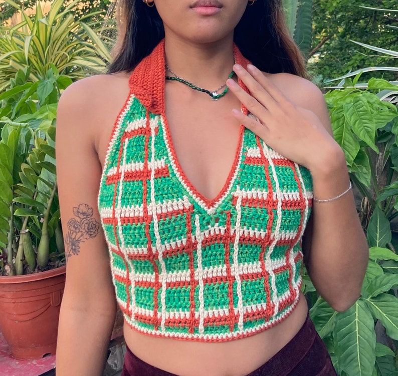 May include: A green and orange crocheted halter top with a white trim. The top has a plaid pattern and a deep V-neck.