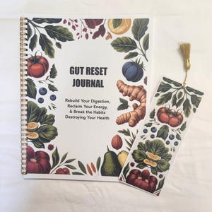 May include: A spiral-bound Gut Reset Journal with a white cover featuring illustrations of tomatoes, blueberries, ginger, and leafy greens. The text reads: Gut Reset Journal, Rebuild Your Digestion, Reclaim Your Energy, & Break the Habits Destroying Your Health. A matching bookmark with a gold tassel is included.