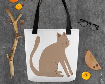 Könnte beinhalten: Eine weiße Einkaufstasche mit schwarzen Henkeln zeigt eine braune Katzenillustration. Die Katze sitzt mit ihrem Schwanz um den Körper gewickelt und schaut nach rechts.