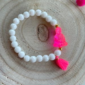Könnte beinhalten: Weißes Perlenarmband mit einem rosafarbenen Buddha-Anhänger und einem rosafarbenen Quaste.