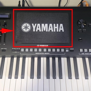 Puede incluir: Un teclado Yamaha negro con teclas blancas y negras. El teclado tiene un panel negro con el logotipo y el texto de Yamaha en blanco. Incluye varios botones, controles deslizantes y una pantalla.