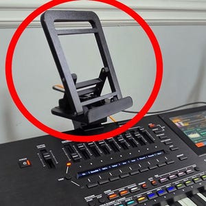 Peut inclure: Un support noir pliable à angle réglable conçu pour maintenir un appareil mobile ou une tablette. Le support présente un cadre rectangulaire avec une barre de support horizontale et un rebord inférieur, fabriqué en plastique noir mat.