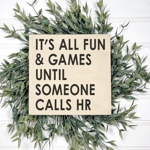 May include: A wooden sign with the text "It's all fun & games until someone calls HR". The sign is light brown and the text is black.