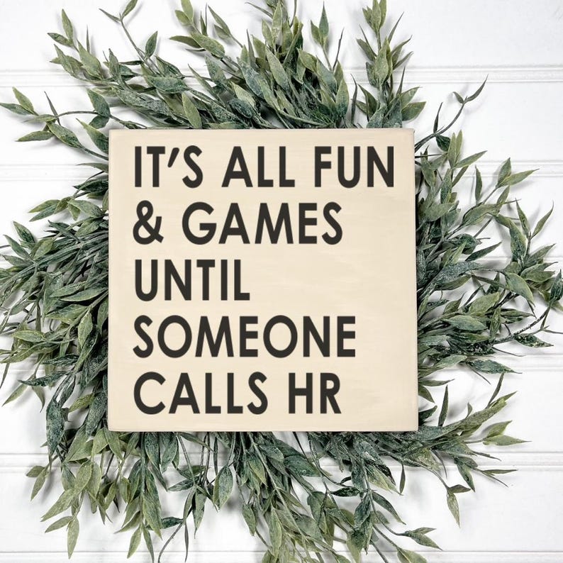 May include: A wooden sign with the text "It's all fun & games until someone calls HR". The sign is light brown and the text is black.