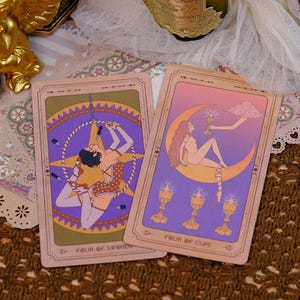 K&ouml;nnte beinhalten: Zwei Tarotkarten mit Illustrationen. Eine Karte zeigt eine Figur in einem Reifen, die andere eine Frau auf einem Halbmond. Die Karten haben einen Vintage-Stil mit dem Text "Four of Swords" und "Four of Cups".