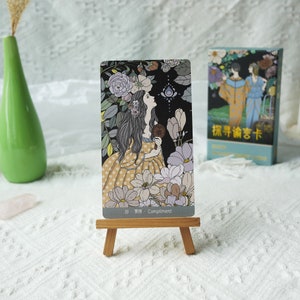 May include: A tarot card with a woman in a yellow dress with white polka dots standing in a garden. The card is titled "19. Compliment".