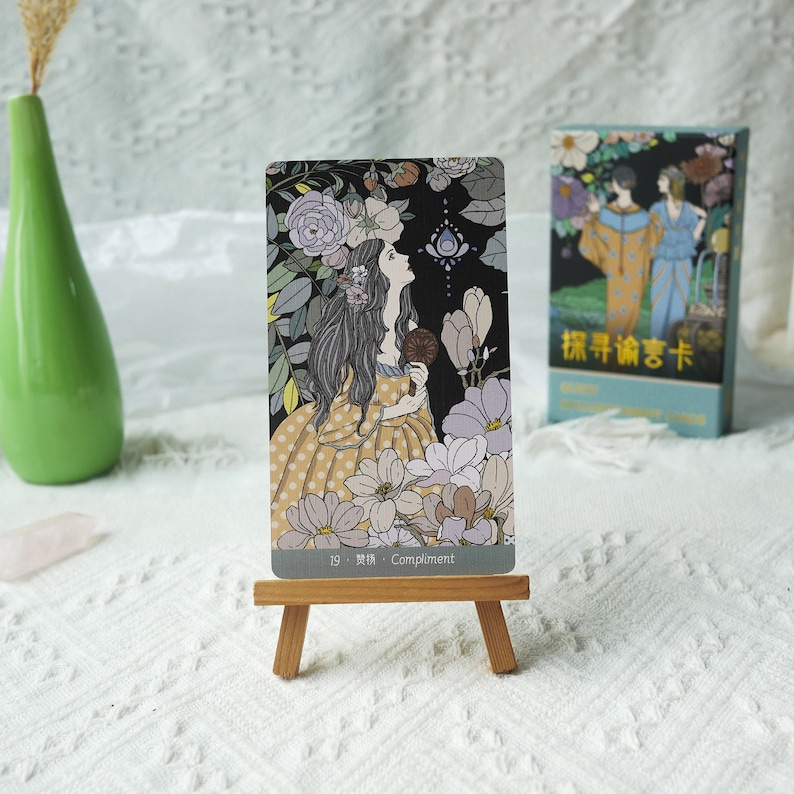 May include: A tarot card with a woman in a yellow dress with white polka dots standing in a garden. The card is titled "19. Compliment".