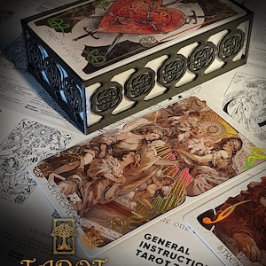 May include: A tarot card deck with a decorative box. The box features Celtic knot designs and the words "THREE OF SWORDS." The cards display detailed illustrations, including the "JUDGEMENT" and "STRENGTH" cards. The deck is labeled "TAROT The Forest Knows."