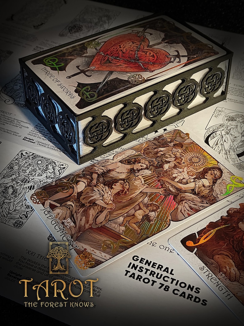 May include: A tarot card deck with a decorative box. The box features Celtic knot designs and the words "THREE OF SWORDS." The cards display detailed illustrations, including the "JUDGEMENT" and "STRENGTH" cards. The deck is labeled "TAROT The Forest Knows."