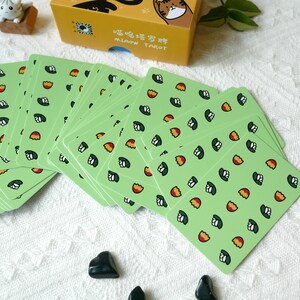Puede incluir: Una baraja de cartas de tarot verde con un patr&oacute;n de flores blancas y huevos naranjas. La caja de las cartas est&aacute; en el fondo y dice "喵喵塔羅 MIAOW TAROT" en chino e ingl&eacute;s.