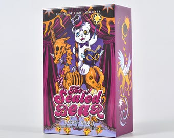 May include: A tarot card box with a whimsical illustration. The box features a cartoon bear in a top hat holding a wand and book, with the text "The Sealed Bear Tarot Card". The box has a purple and gold colour scheme.
