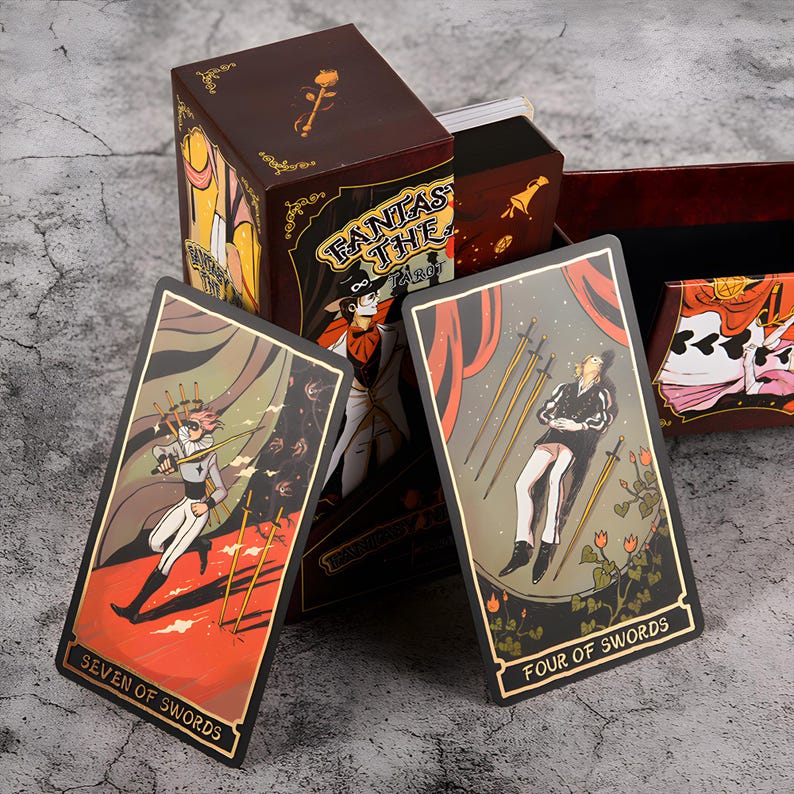May include: A tarot card deck with a brown box featuring the text "FANTASY THE TAROT". Two tarot cards are visible, one labeled "SEVEN OF SWORDS" and the other "FOUR OF SWORDS". The cards have gold borders and detailed illustrations.