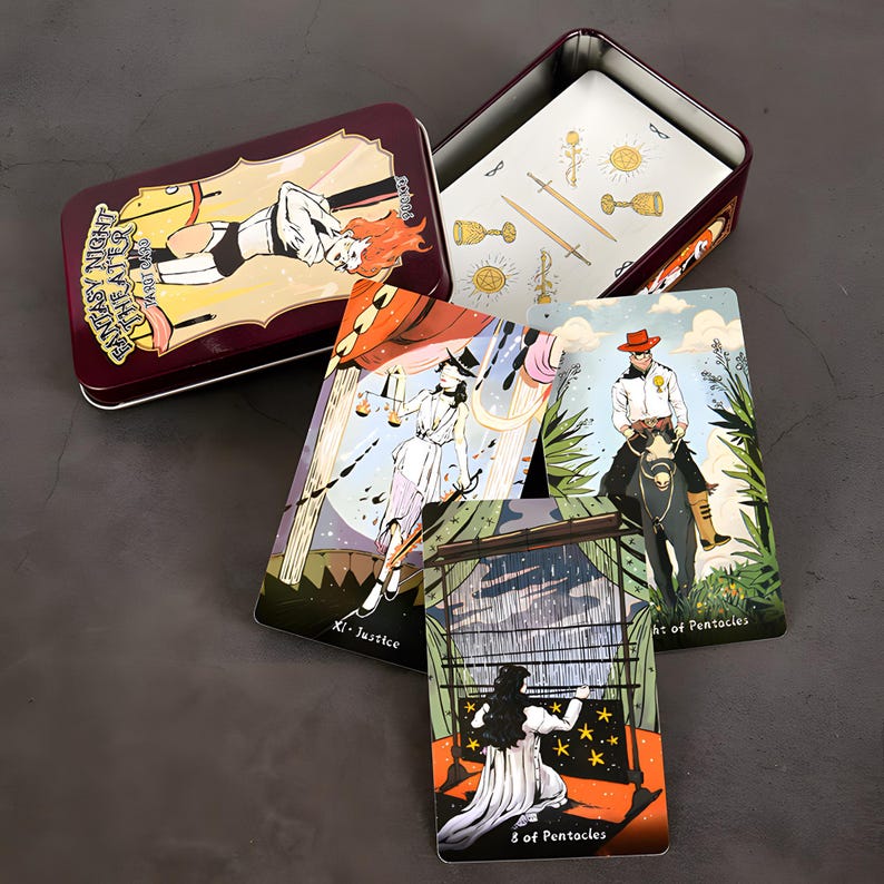 May include: A tarot card set featuring illustrated cards and a burgundy metal tin. The tin has an illustration of a person with red hair. Several cards are visible, including the Justice and 8 of Pentacles cards.