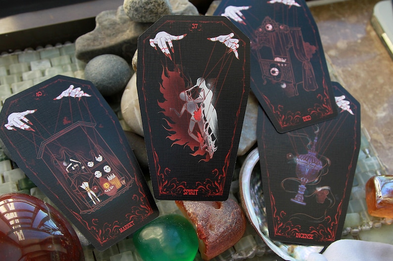 May include: Four coffin-shaped cards with black backgrounds and red line art illustrations. The cards feature marionette hands, a figure labeled Spirit, a market scene, and an incense burner. Each card has a unique number and text at the bottom.
