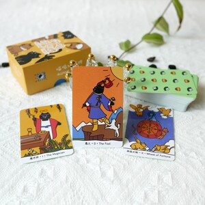 Puede incluir: Tres cartas de tarot con gatos negros sobre un fondo blanco. Las cartas son amarillas, naranjas y azules con contornos negros. Las cartas est&aacute;n etiquetadas como "El Mago", "El Loco" y "La Rueda de la Fortuna".