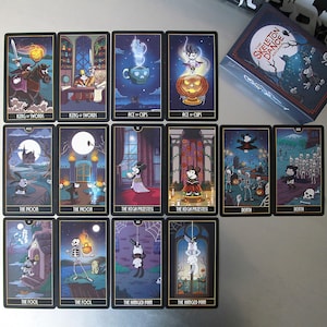 May include: A deck of tarot cards with a Halloween theme. Each card features a unique illustration with characters and symbols. The box reads "The Skeleton Dance Arcana". The cards are displayed on a light gray surface.