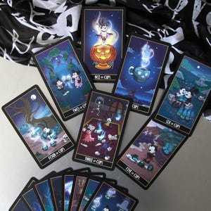 May include: A collection of tarot cards featuring cartoon characters in a Halloween theme. The cards have a black border and depict various scenes with characters, including "Ace of Cups," "Two of Cups," and "Six of Cups."