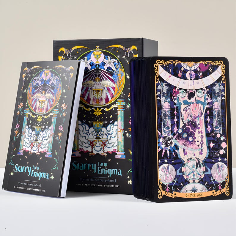 May include: A tarot card deck and guidebook set. The box, book, and cards feature a dark background with colorful illustrations of celestial and mystical themes. The text "Starry Enigma" is visible on the box and book. The card deck shows "O The Fool".