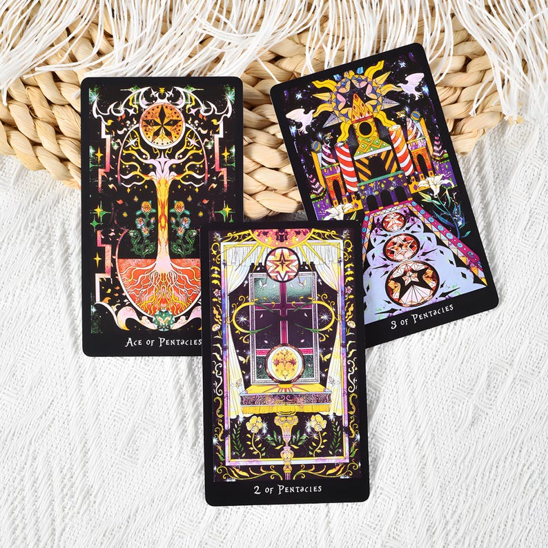 May include: Three tarot cards with intricate illustrations are displayed. The cards feature vibrant colors and detailed artwork, including images of a tree, a window, and a celestial design. The cards are labeled "Ace of Pentacles", "2 of Pentacles", and "3 of Pentacles".