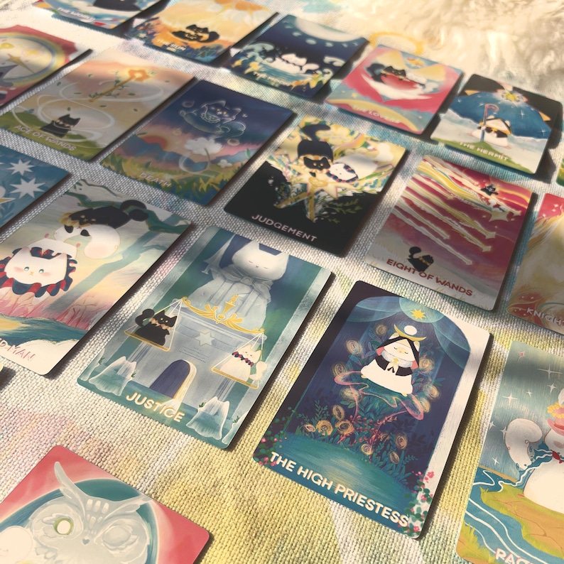 K&ouml;nnte beinhalten: Eine Sammlung rechteckiger Tarotkarten mit farbenfrohen Illustrationen von Katzen in verschiedenen Posen und Umgebungen. Sichtbarer Text umfasst The High Priestess, Justice, Judgement, Eight of Wands und Ace of Cups auf den Kartenoberfl&auml;chen.