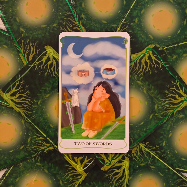 May include: A tarot card illustration featuring a woman in an orange dress dreaming of cat food, with a white cat and two swords. The card is labeled "TWO OF SWORDS" and set against a background of green foliage.
