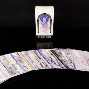 May include: A deck of cards with a white box featuring a purple and blue illustration of a person in the clouds. The box has the text "MONSOON" on the front.